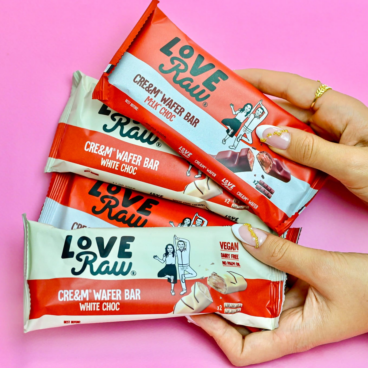 Hands holding LoveRaw cream wafer bars against a pink background